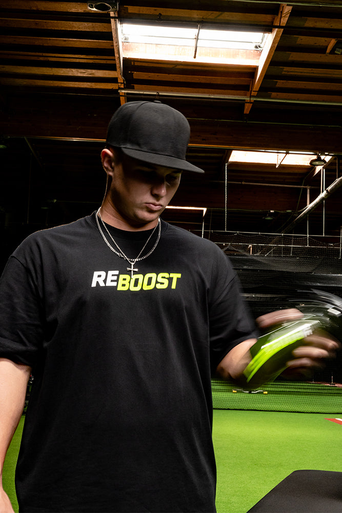 Jaxon Willits wearing a black t-shirt with 'REBOOST' printed in white and yellow on the chest, standing in an indoor sports facility and holding a green disc.