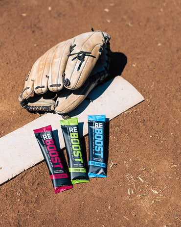 Baseball glove and REBOOST energy stick packs on a baseball base with dirt background