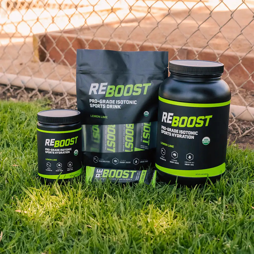 REBOOST sports drink products on grass with a chain-link fence in the background