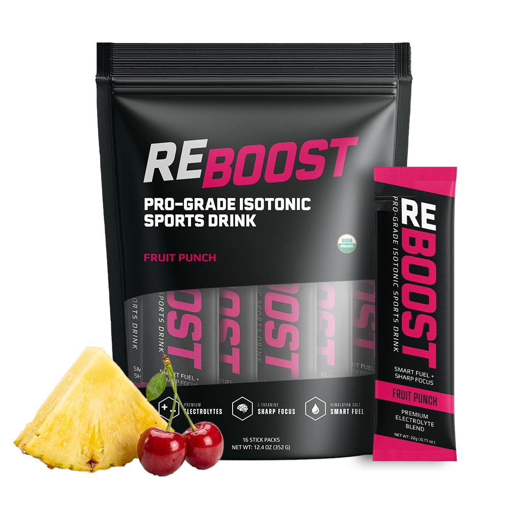 RE BOOST Pro-Grade Isotonic Sports Drink in Fruit Punch flavor, shown as a large black resealable pouch with a matching single stick pack standing beside it, plus a pineapple wedge and two cherries as flavor cues on a white background.