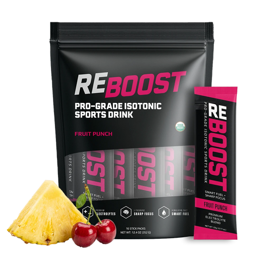 RE BOOST Pro-Grade Isotonic Sports Drink in Fruit Punch flavor, shown as a large black resealable pouch with a matching single stick pack standing beside it, plus a pineapple wedge and two cherries as flavor cues on a white background.